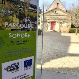 En premier plan, l'affiche du parcours sonore du musée Rabelais attestant de son cofinancement par LEADER. En arrière plan, la maison de la Devinière avec une porte rouge et un petit arbre à droite